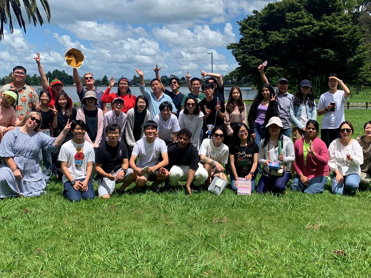 A diverse, cheerful group of international students and teachers posing together outdoors on a sunny day...