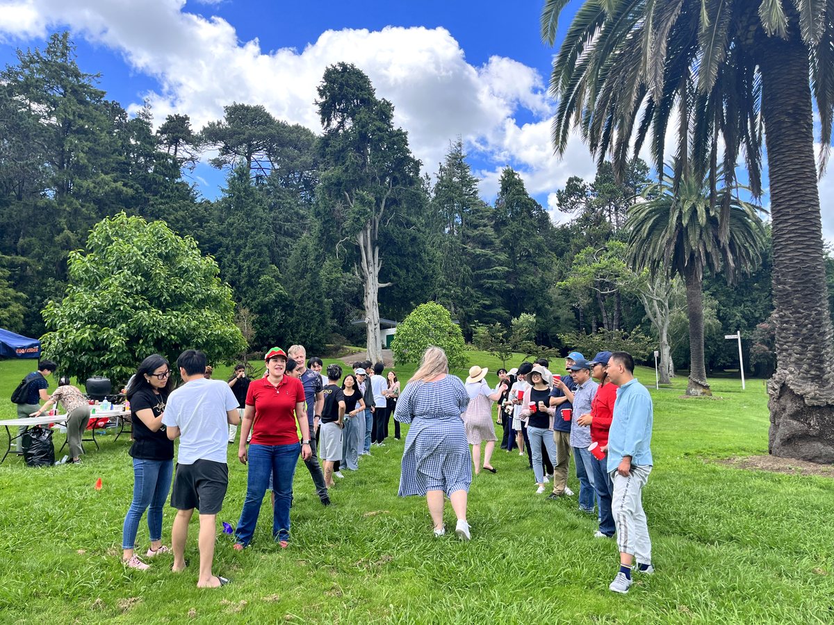 A diverse group of international students and staff enjoying an outdoor social gathering in a lush green...