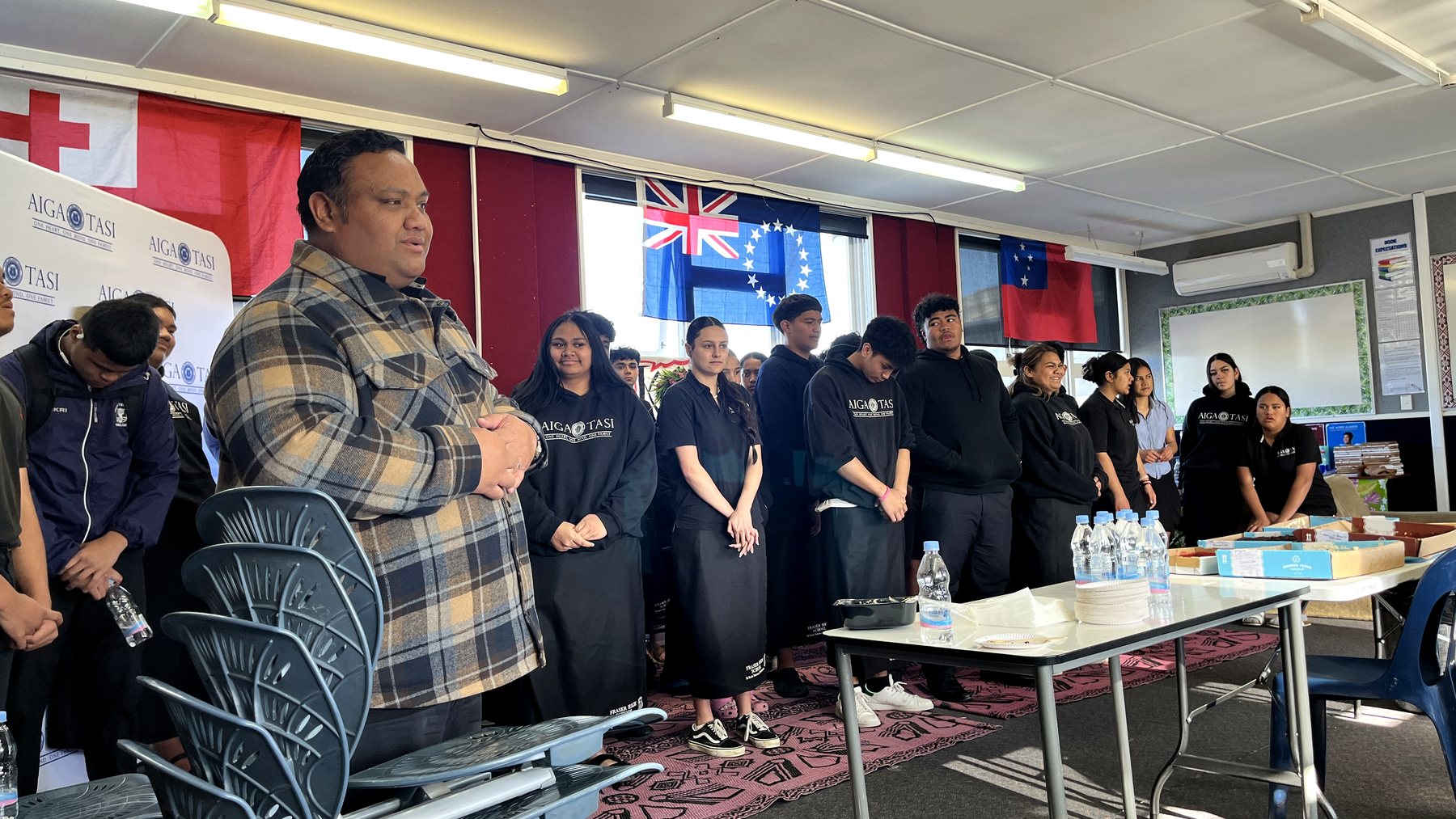 A Pasifika community or high school student group gathered inside a classroom, participating in a solemn...
