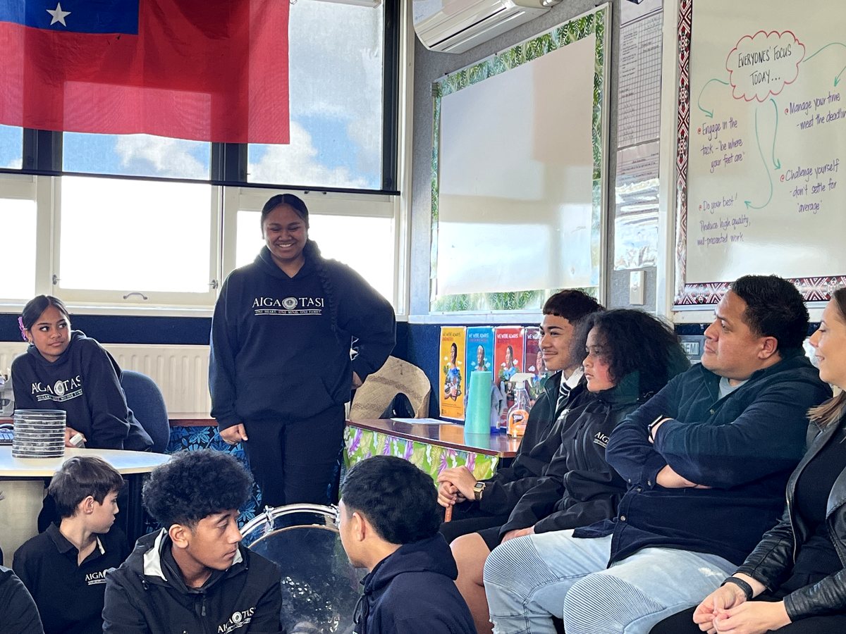 A group of students and staff engaged in a supportive classroom session with cultural elements visible,...