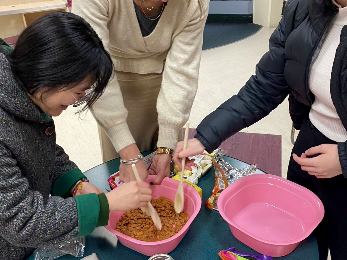 Three female students and a teacher/facilitator actively engaged in a hands-on cultural activity, mixing...
