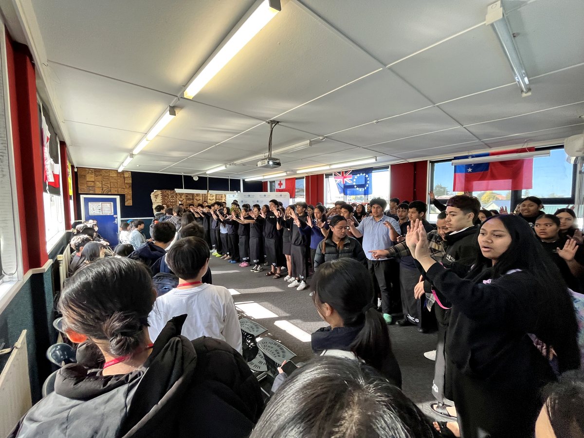 A diverse group of students participating in an indoor cultural activity or performance with raised hands...