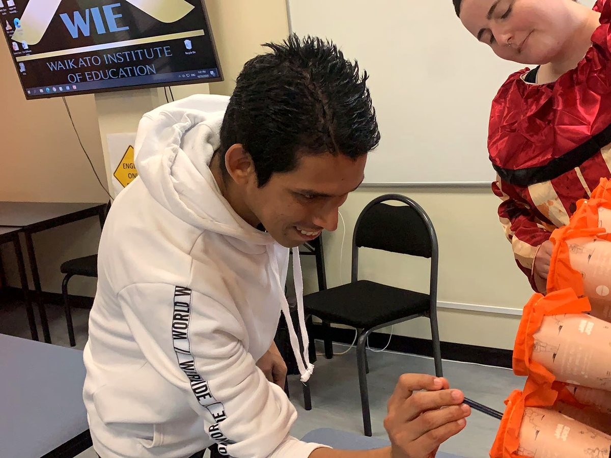 A male student in a white hoodie smiles while engaged in a creative artwork/craft activity in a WIE...