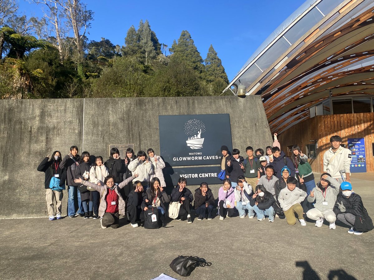 A large group of international students and staff posing cheerfully in front of the Waitomo Glowworm Caves...