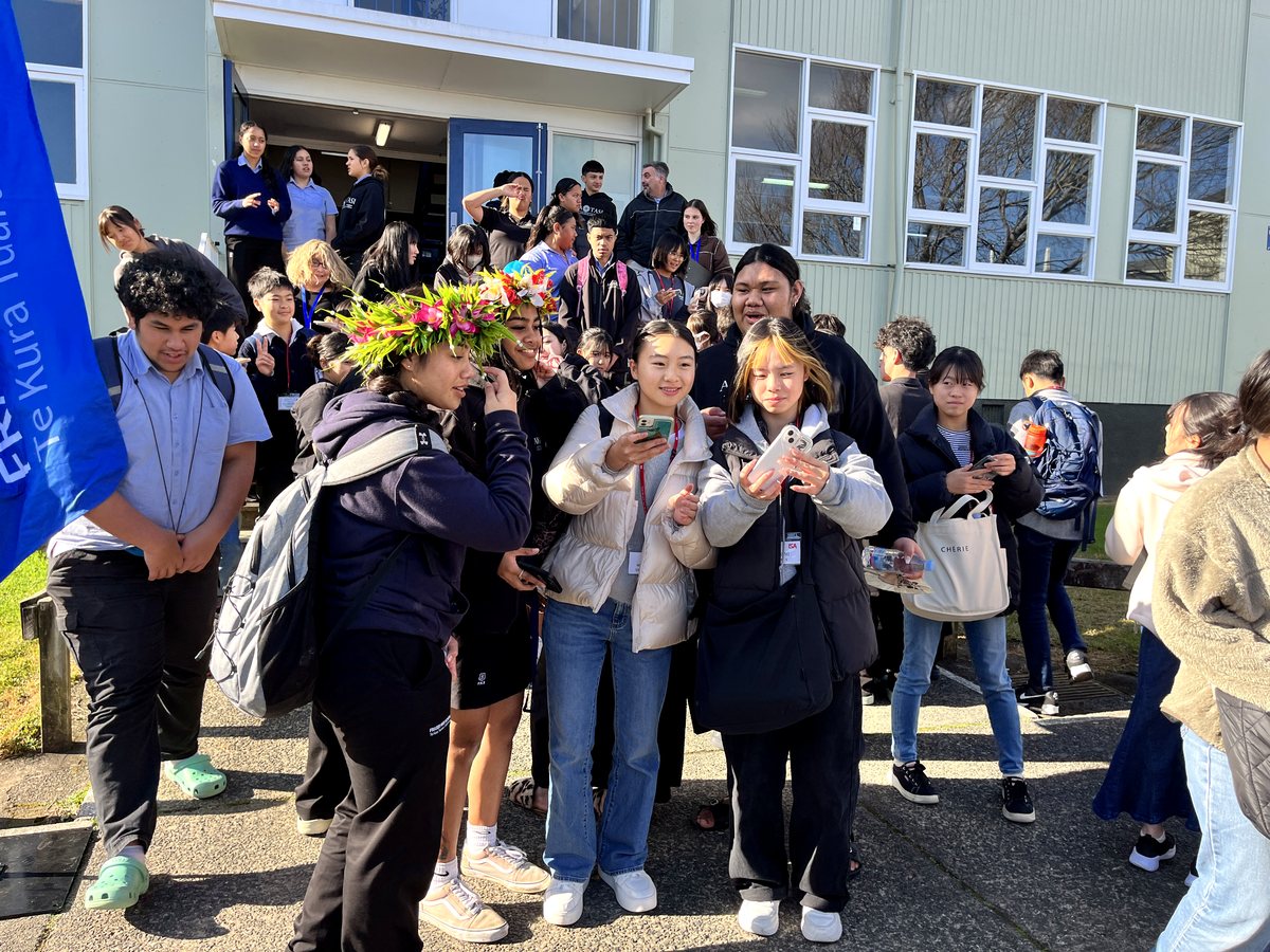A diverse group of international and high school students gathered outside a building entrance during daylight