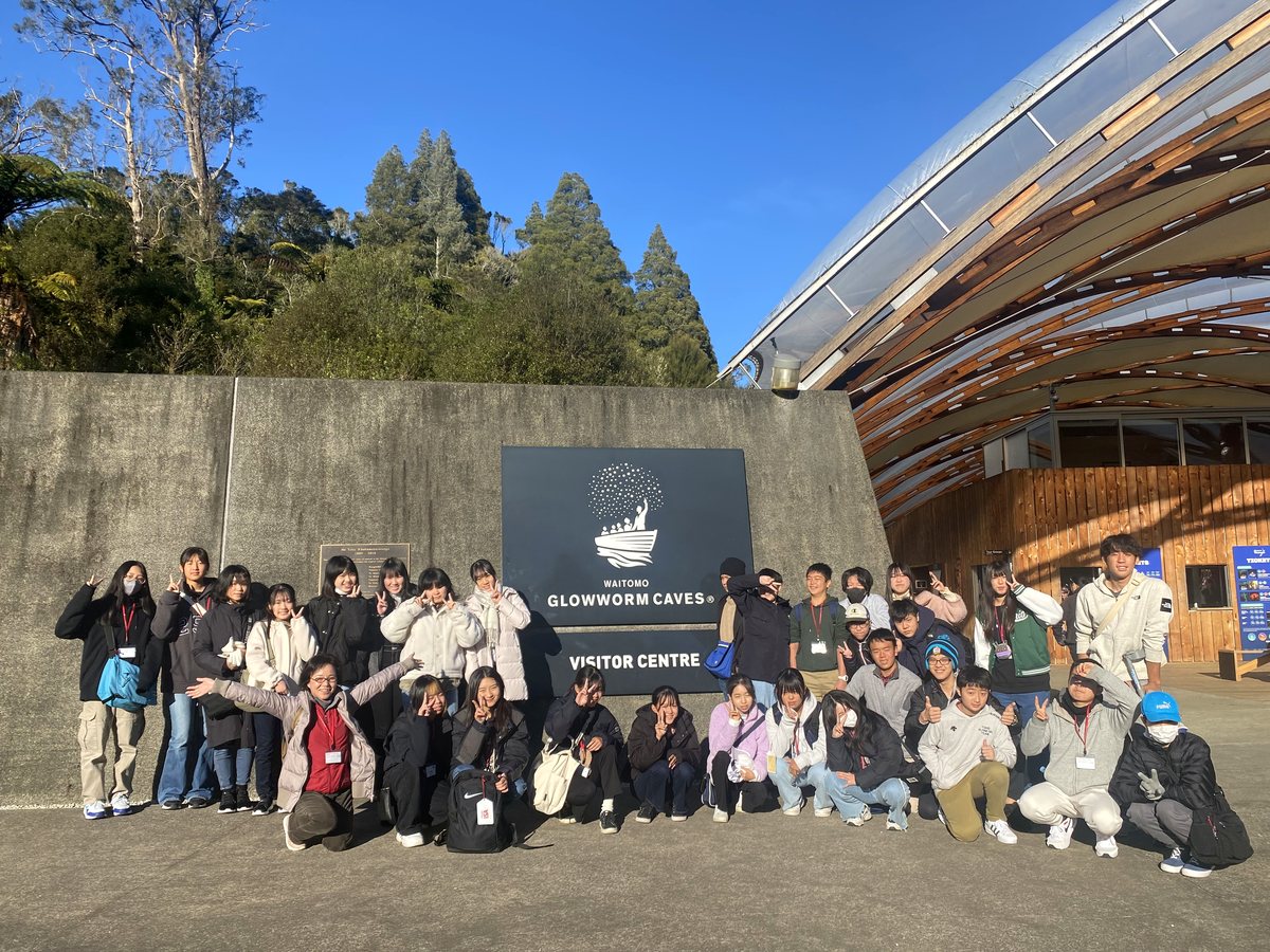 A large group of international students and staff posing enthusiastically in front of the Waitomo Glowworm...