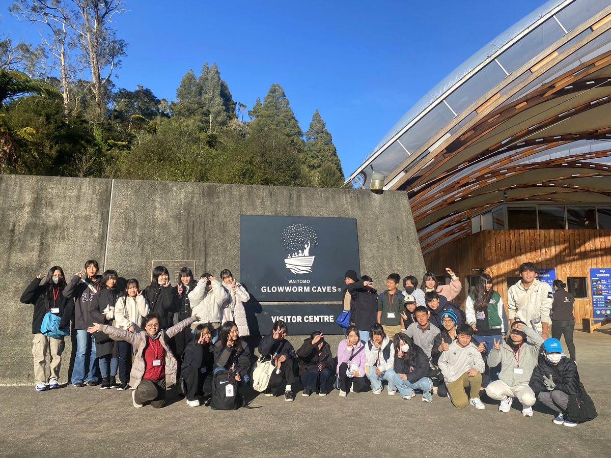 A large, cheerful group of international students and chaperones posing in front of the Waitomo Glowworm...