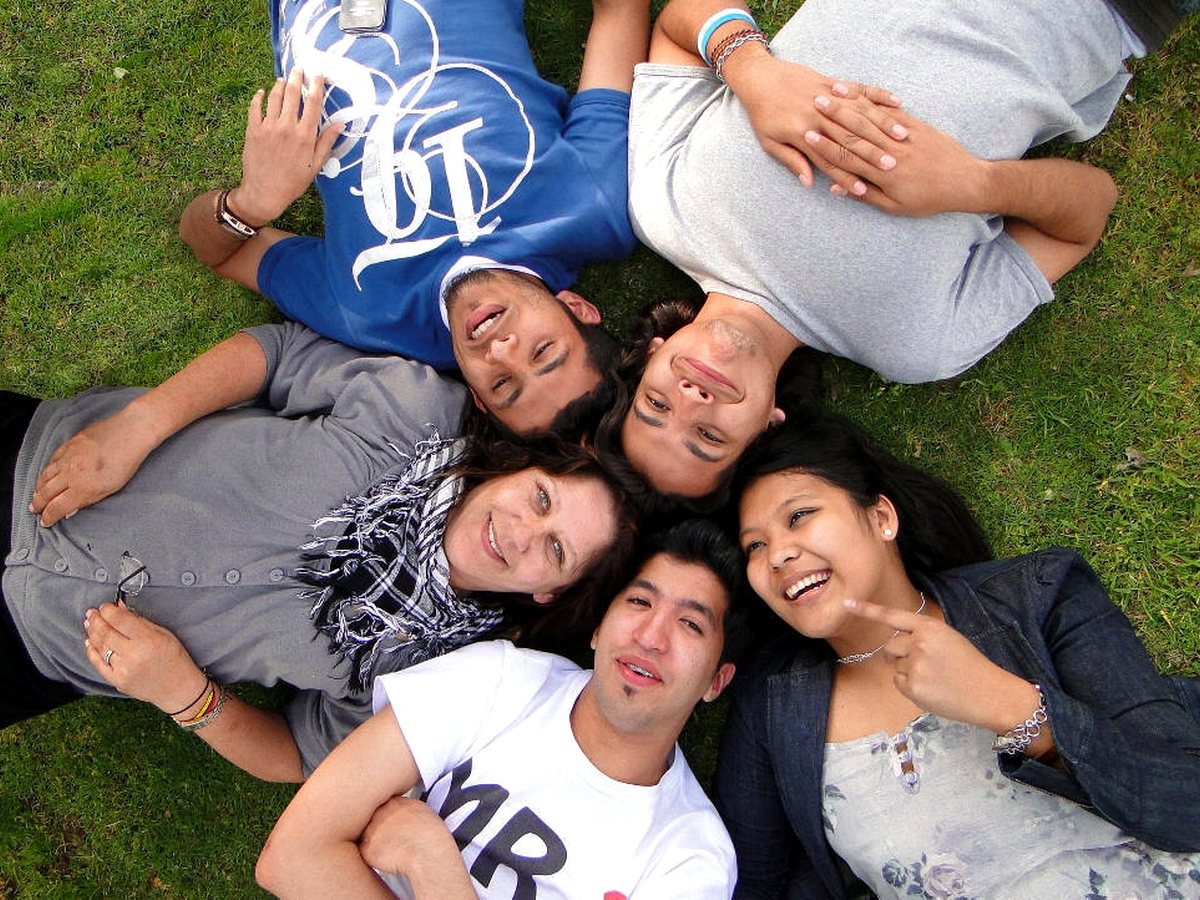 An overhead high-angle shot of five diverse international students lying in a star formation on green...