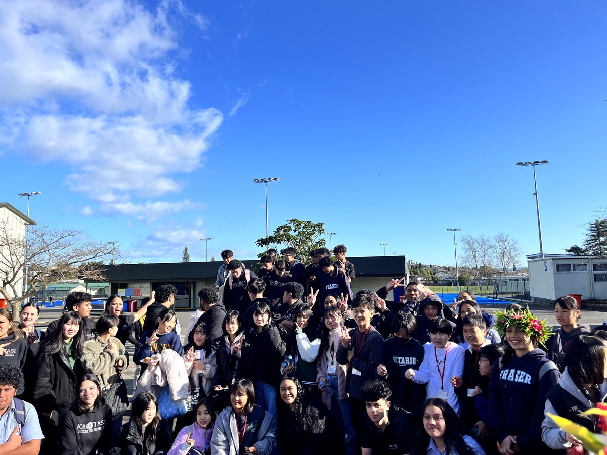 A large, energetic outdoor group photo of young international and local high school students gathered on a...