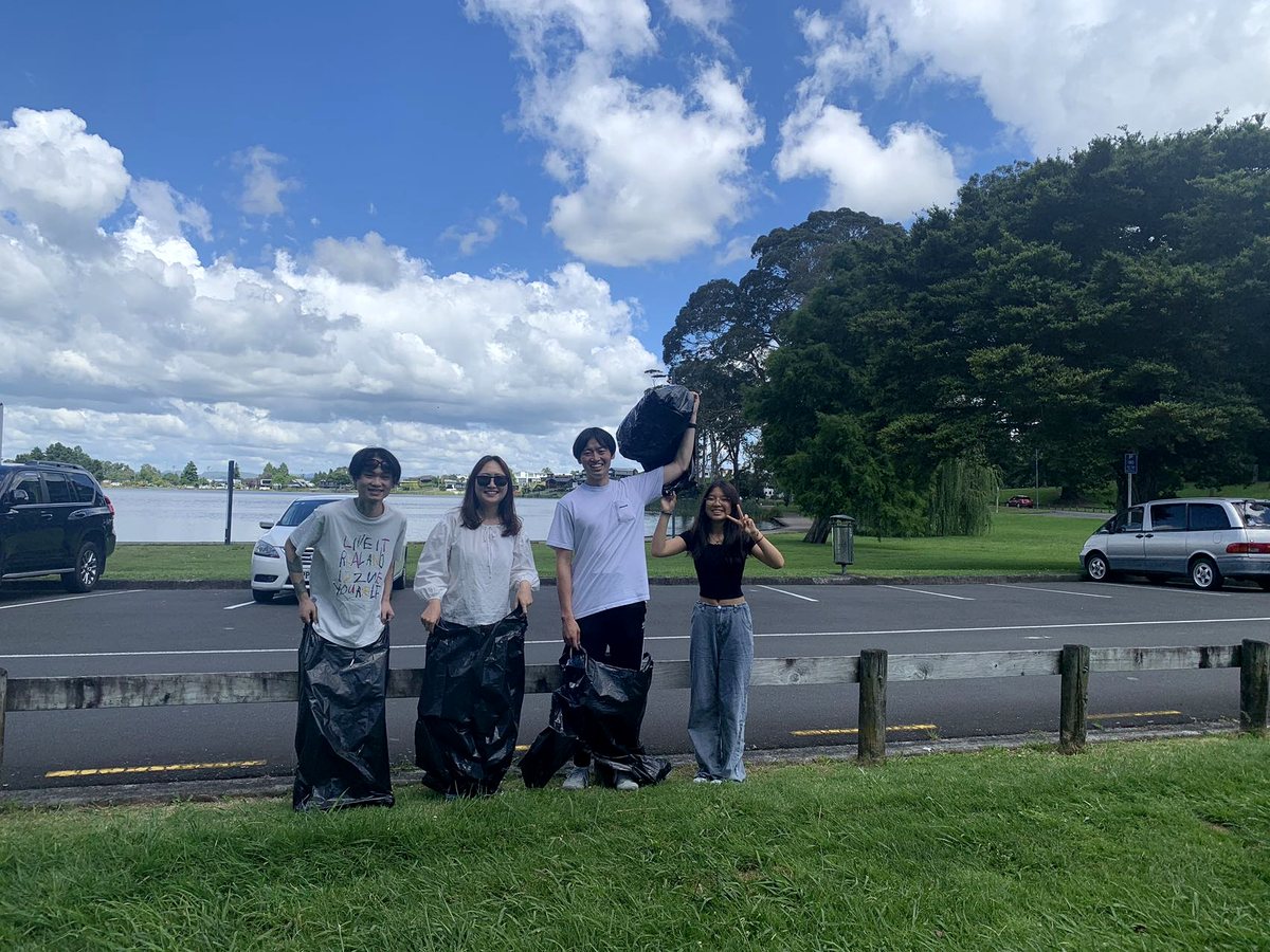 Four international students posing cheerfully with black rubbish bags during a community environmental...