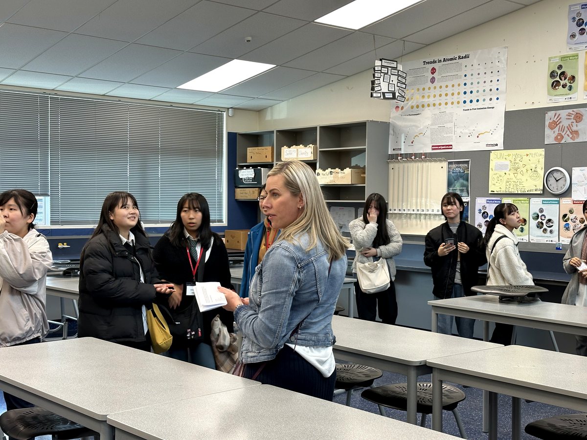 An authentic classroom scene showing an educator interacting with a group of international high school /...