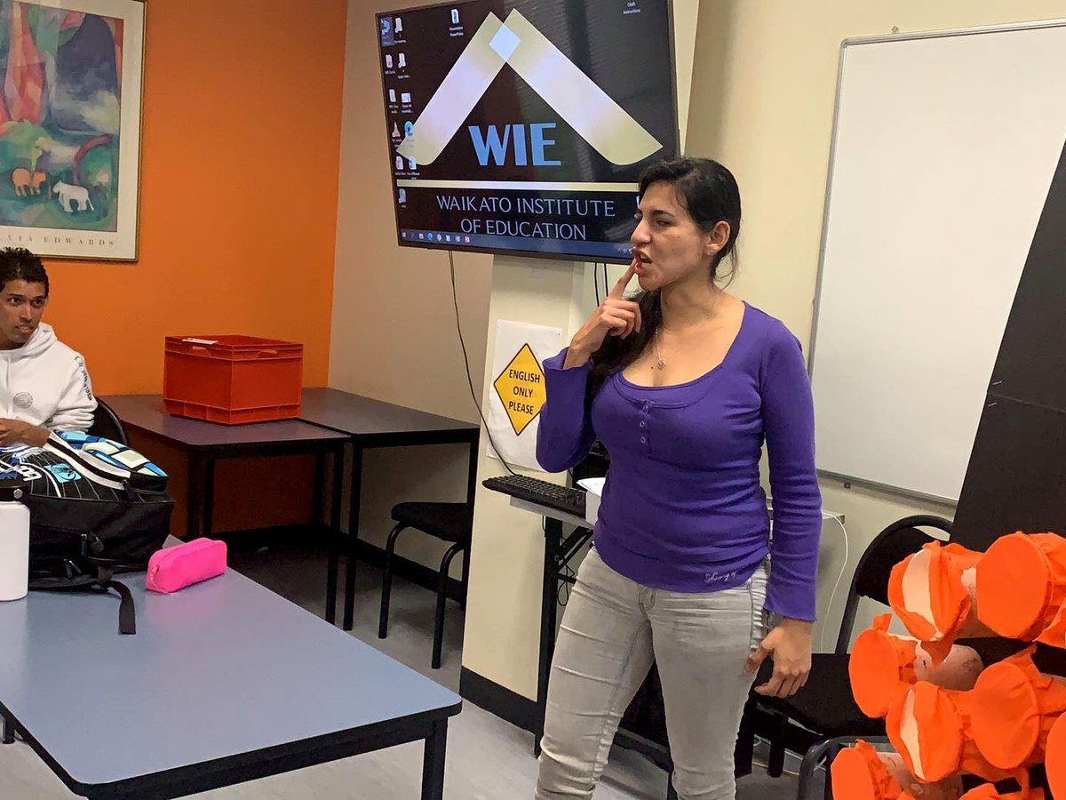 An interactive classroom scene showing a teacher demonstrating English pronunciation in front of a digital...