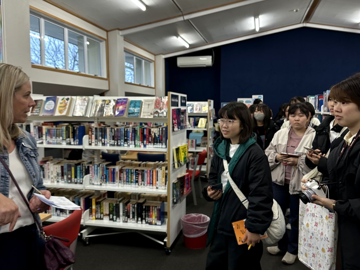 A staff member or teacher speaking with a group of international students during an orientation or library...