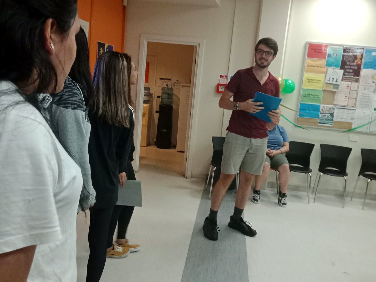Indoor candid shot at WIE campus showing a young male teacher or presenter holding a blue folder and...