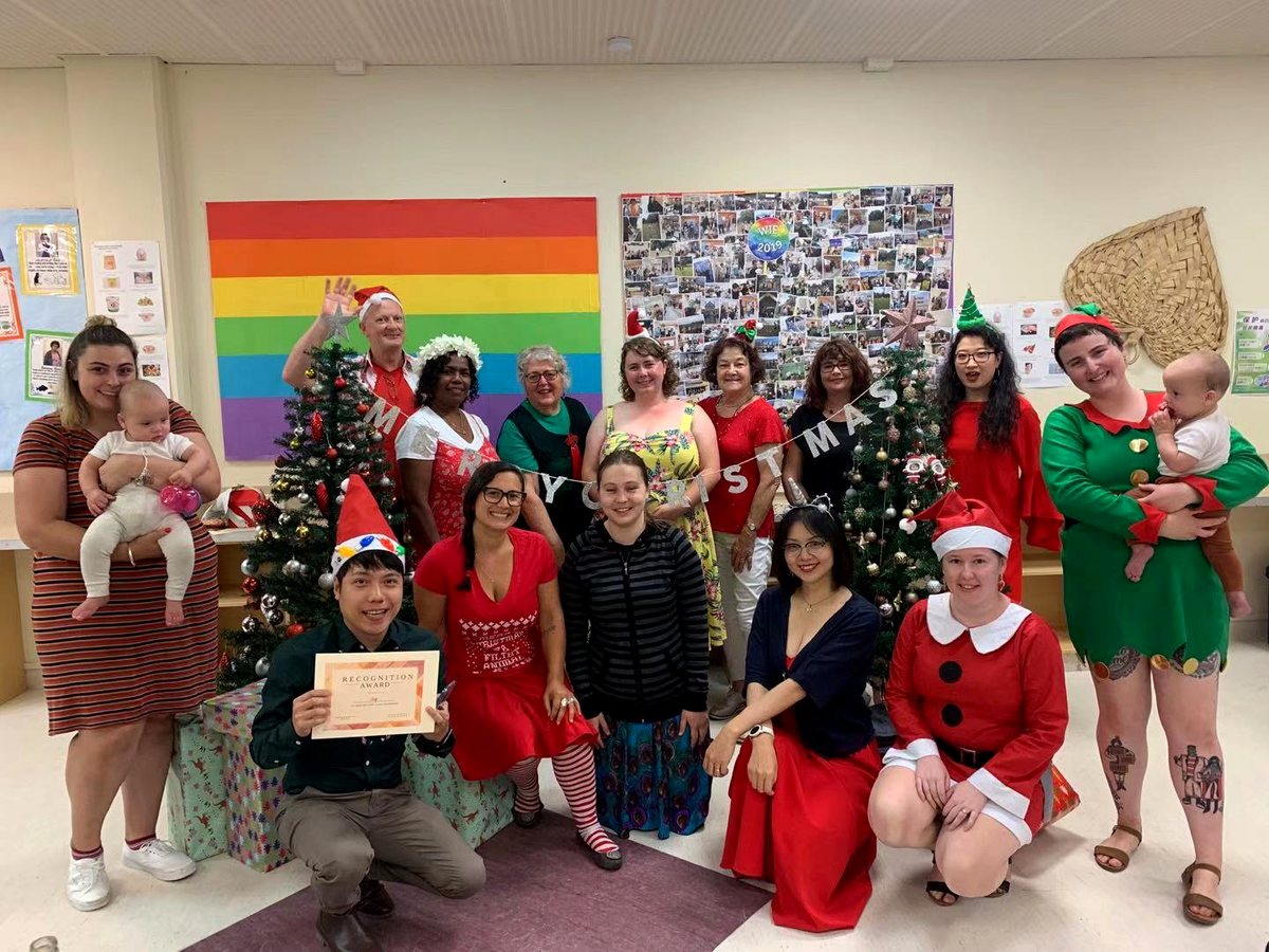 A diverse group of WIE staff and students posing together for a Christmas holiday celebration indoors,...