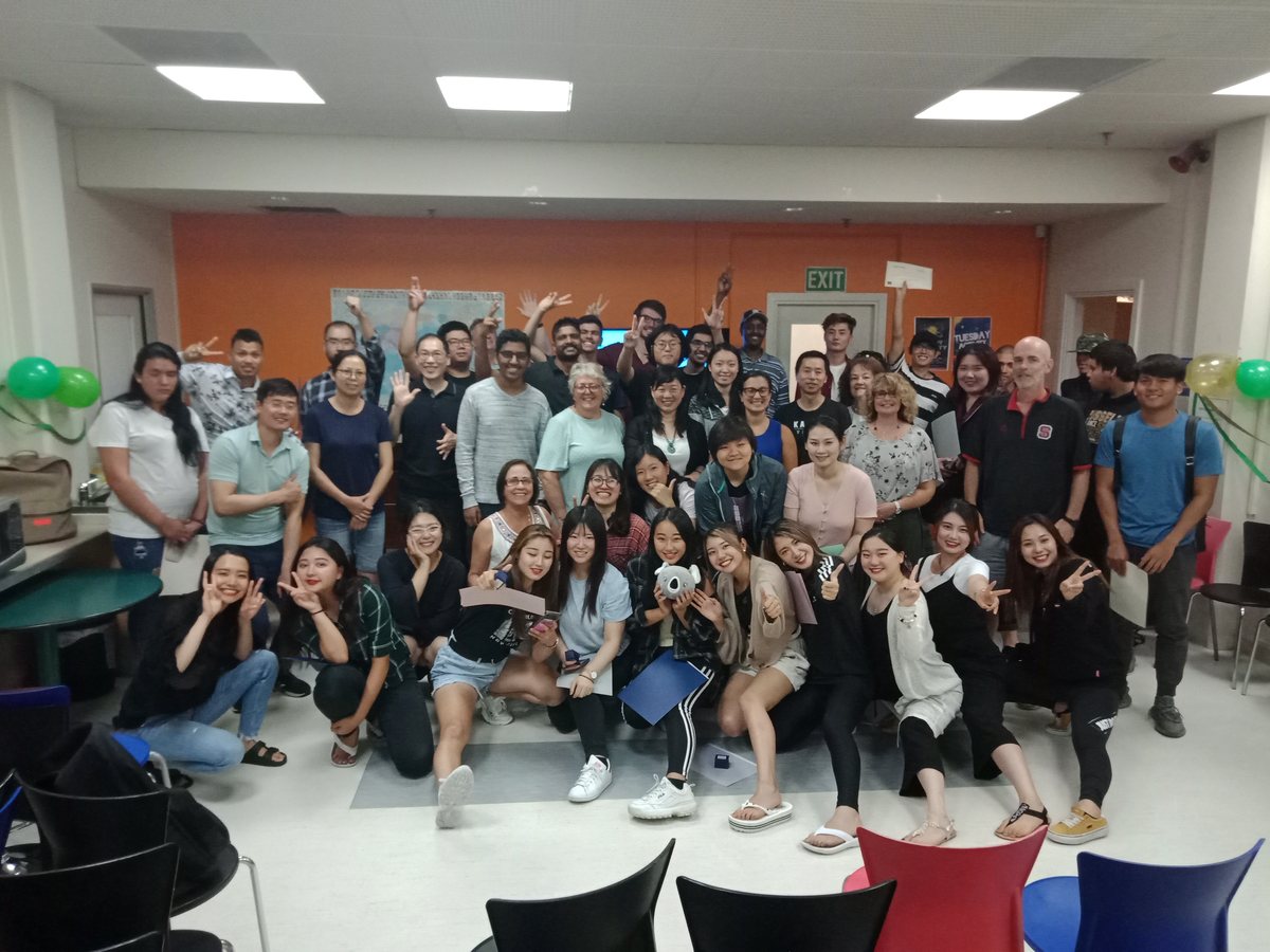 A vibrant indoor group photo featuring a large, diverse group of international students and staff posing...